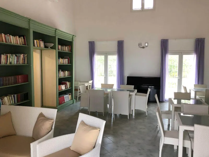Sala comune con libreria verde, tavoli e pianoforte
